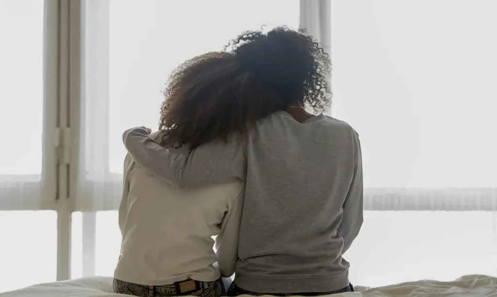 Mom and daughter sitting on bed talking about juvenile defense case and the lawyer that will help them.